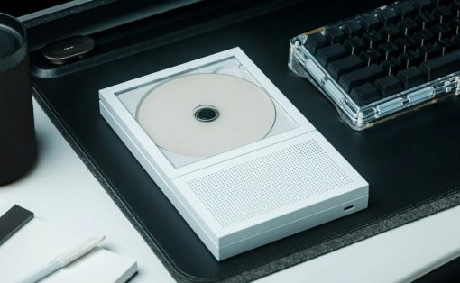 White portable CD player with a disc loaded, sitting on a desk next to a translucent keyboard.