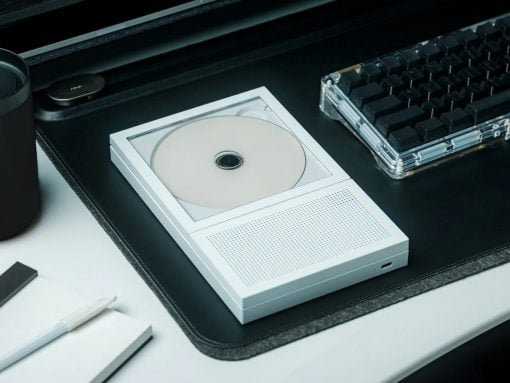 White portable CD player with a disc loaded, sitting on a desk next to a translucent keyboard.