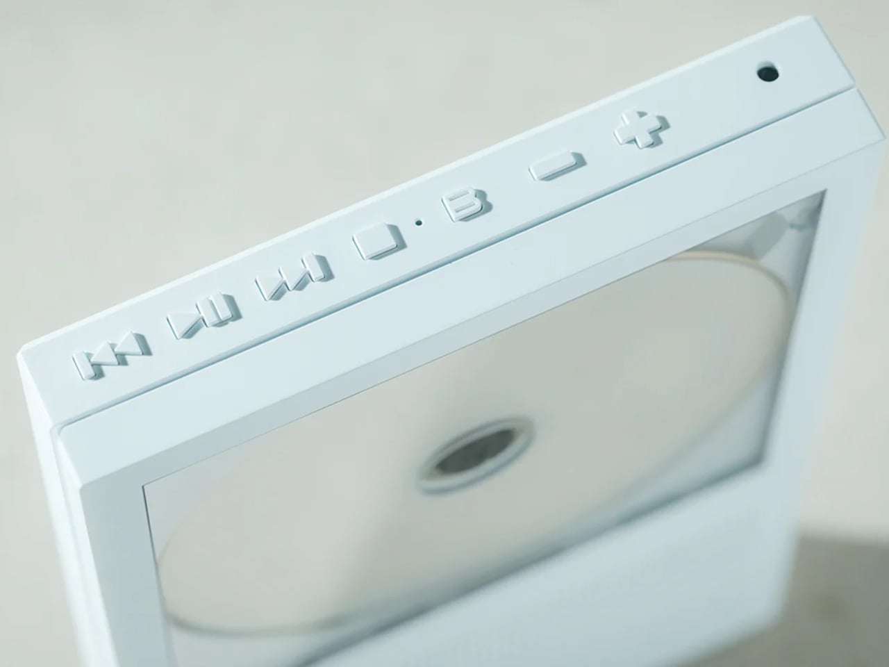 Close-up of a white media drive with a circular disc in the tray and embossed buttons along the top edge.