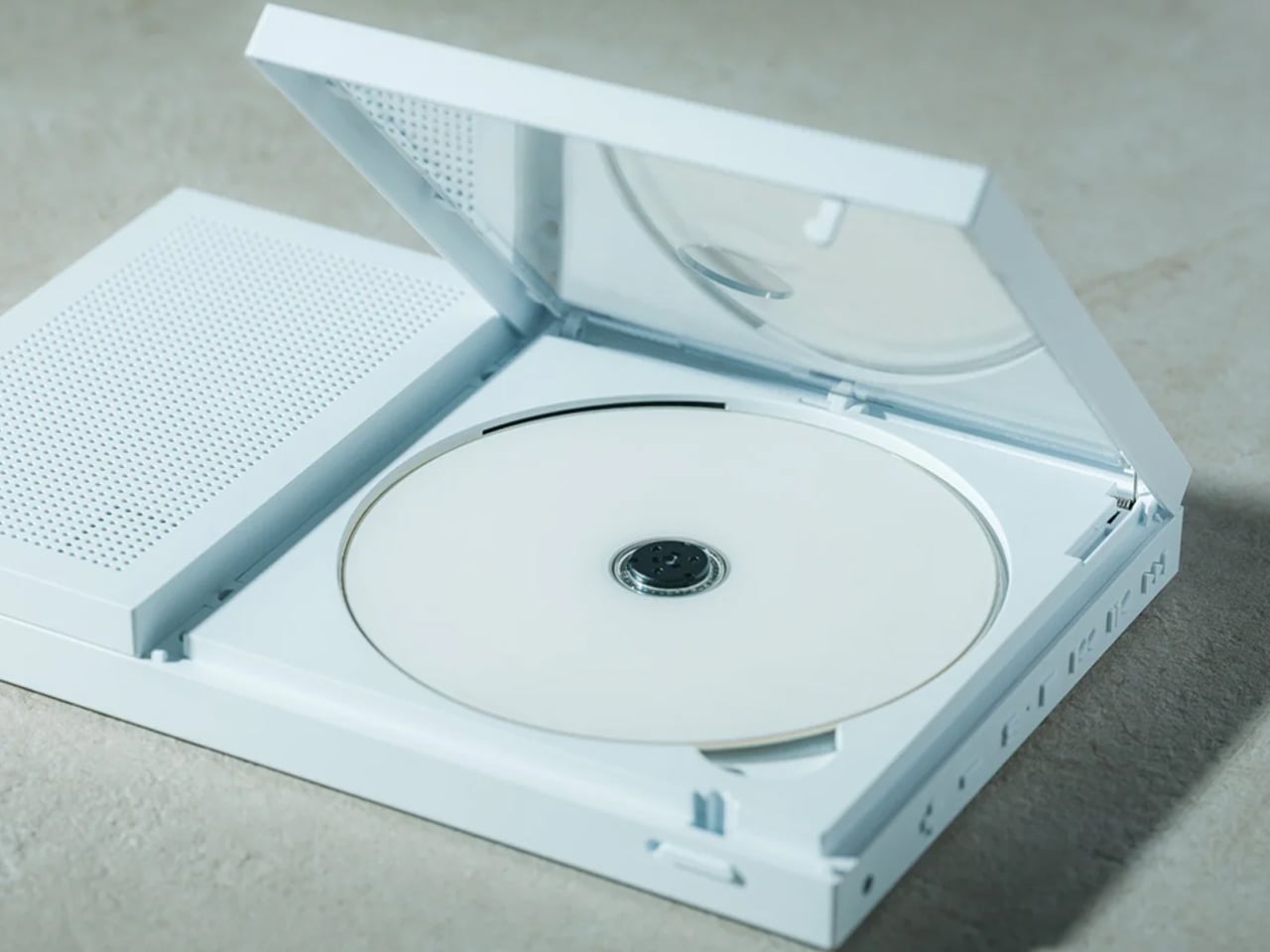 Open white CD/DVD drive with a blank disc in the tray on a light surface