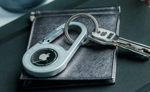 Close-up of a silver circular padlock with keys on a textured dark wallet, highlighting security accessories on a desk surface.