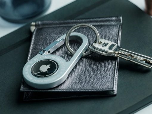 Close-up of a silver circular padlock with keys on a textured dark wallet, highlighting security accessories on a desk surface.