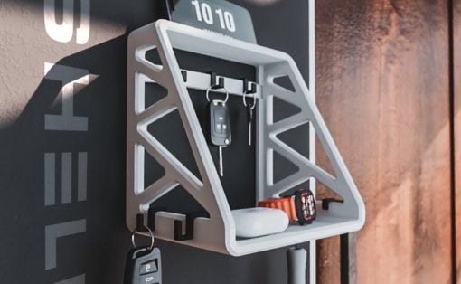 White geometric wall-mounted key shelf holding car keys and other keys on a dark wall