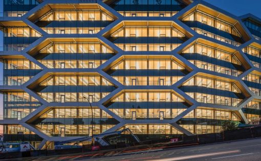 Modern office building with a hexagonal grid facade, illuminated windows at dusk.