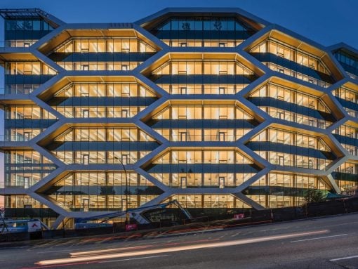 Modern office building with a hexagonal grid facade, illuminated windows at dusk.
