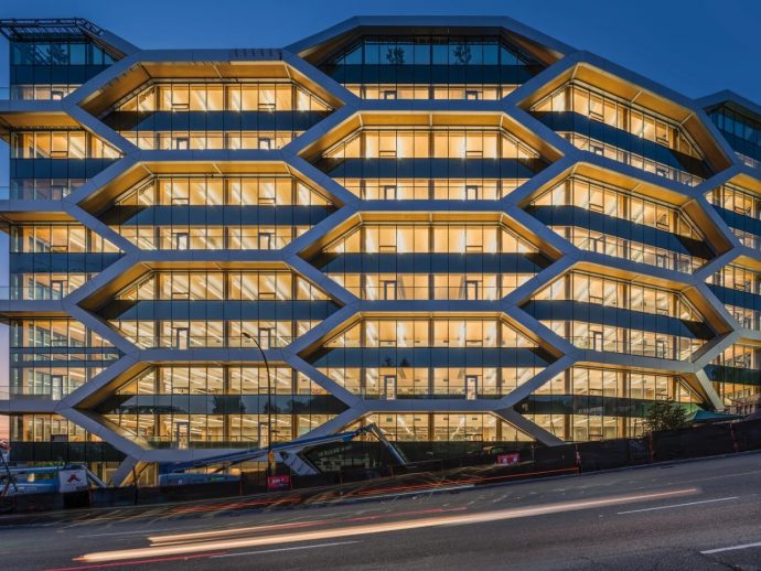 Modern office building with a hexagonal grid facade, illuminated windows at dusk.