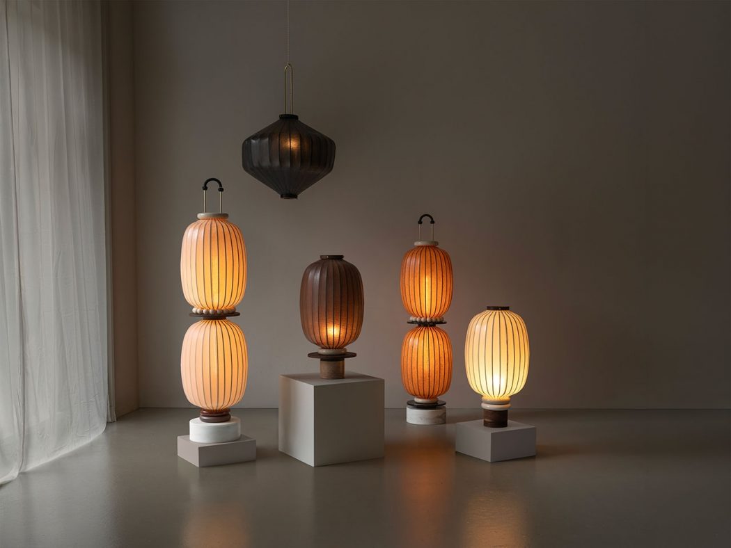 A group of five lantern-style lamps on white pedestals in a dim, minimalist room with sheer curtains on the left, warm amber glow.