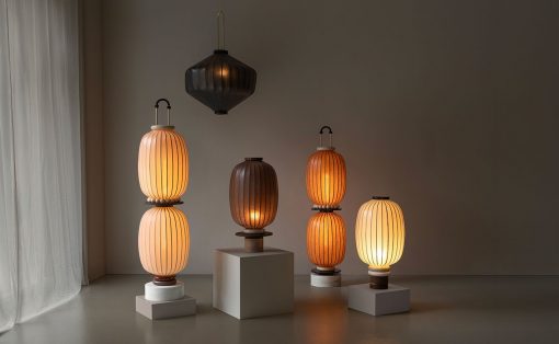 A group of five lantern-style lamps on white pedestals in a dim, minimalist room with sheer curtains on the left, warm amber glow.