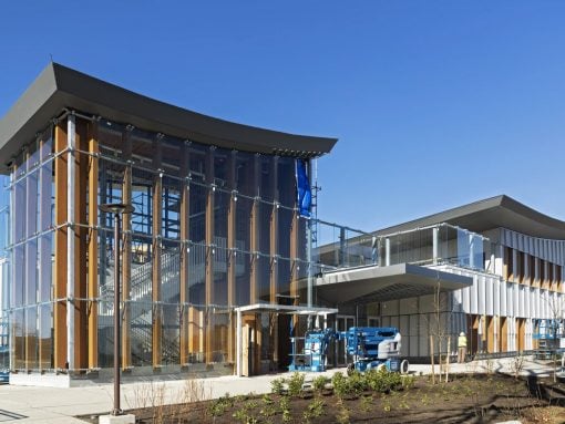 Modern glass-and-wood building under construction with scaffolding and a blue sky backdrop.