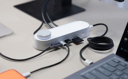 White USB-C hub/dock on a desk with multiple cables plugged in, connected to a laptop nearby.
