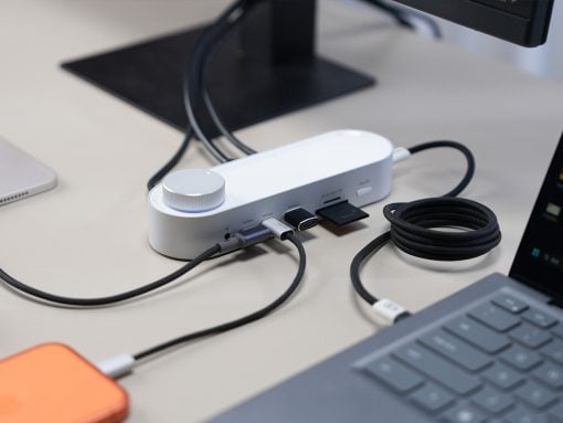 White USB-C hub/dock on a desk with multiple cables plugged in, connected to a laptop nearby.
