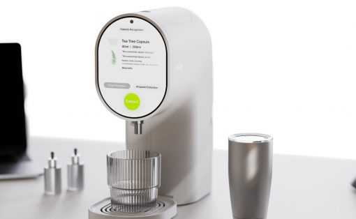 White, modern coffee machine with a circular touchscreen, brewing into a glass cup on a white desk.