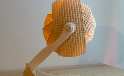 Orange ribbed spherical lamp shade on a white curved arm, resting on a light wood table.