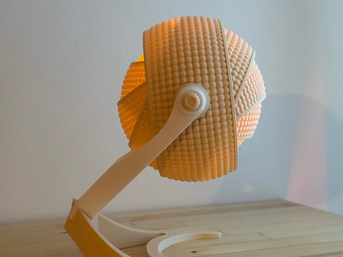 Orange ribbed spherical lamp shade on a white curved arm, resting on a light wood table.