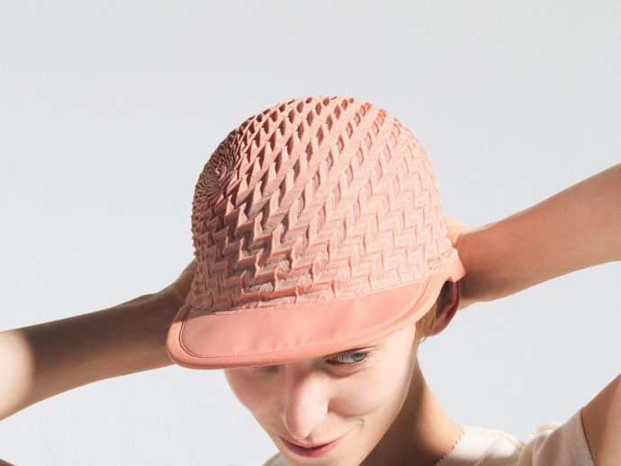 Person wearing a pink woven hat, tilting their head as it’s adjusted by their hands there.