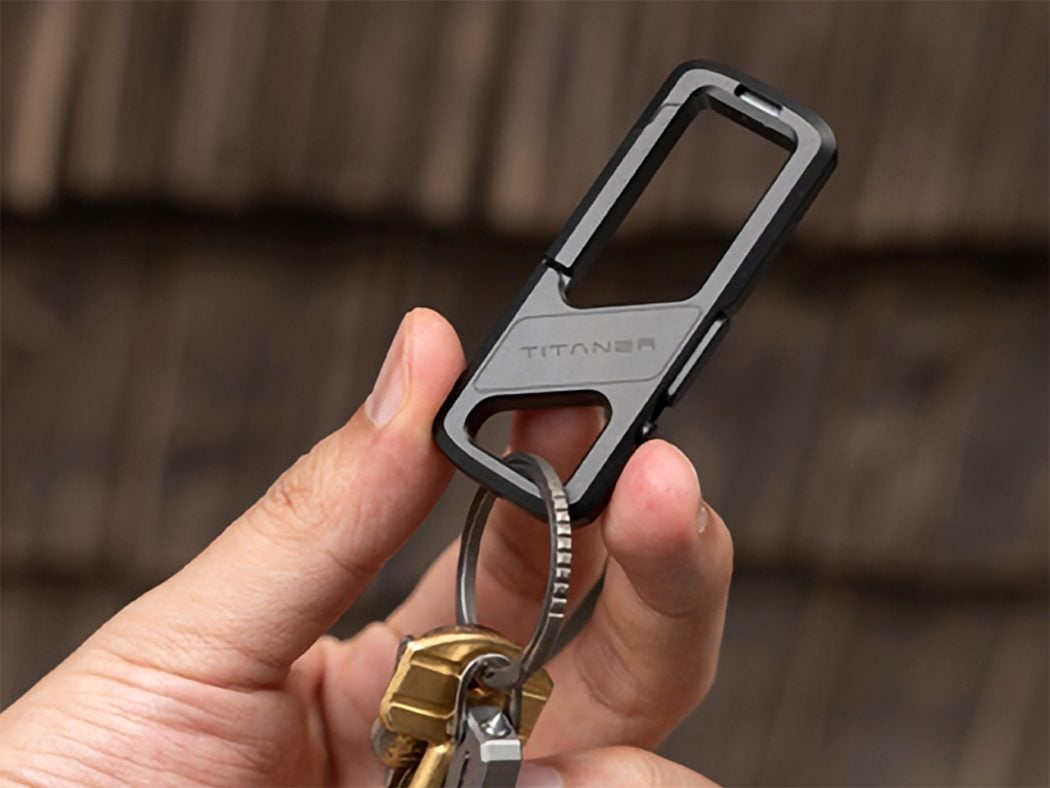 Close-up of a hand holding a gray and black Titan phone-case clip with a key ring attached to several keys.
