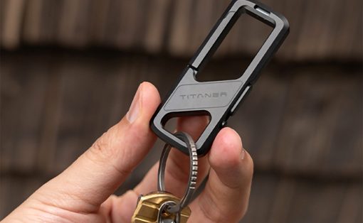 Close-up of a hand holding a gray and black Titan phone-case clip with a key ring attached to several keys.