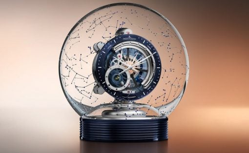 Intricate skeleton wristwatch inside a clear glass globe, with blue constellation lines, mounted on a dark blue ribbed base.
