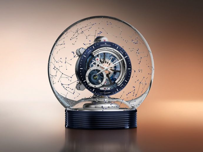 Intricate skeleton wristwatch inside a clear glass globe, with blue constellation lines, mounted on a dark blue ribbed base.