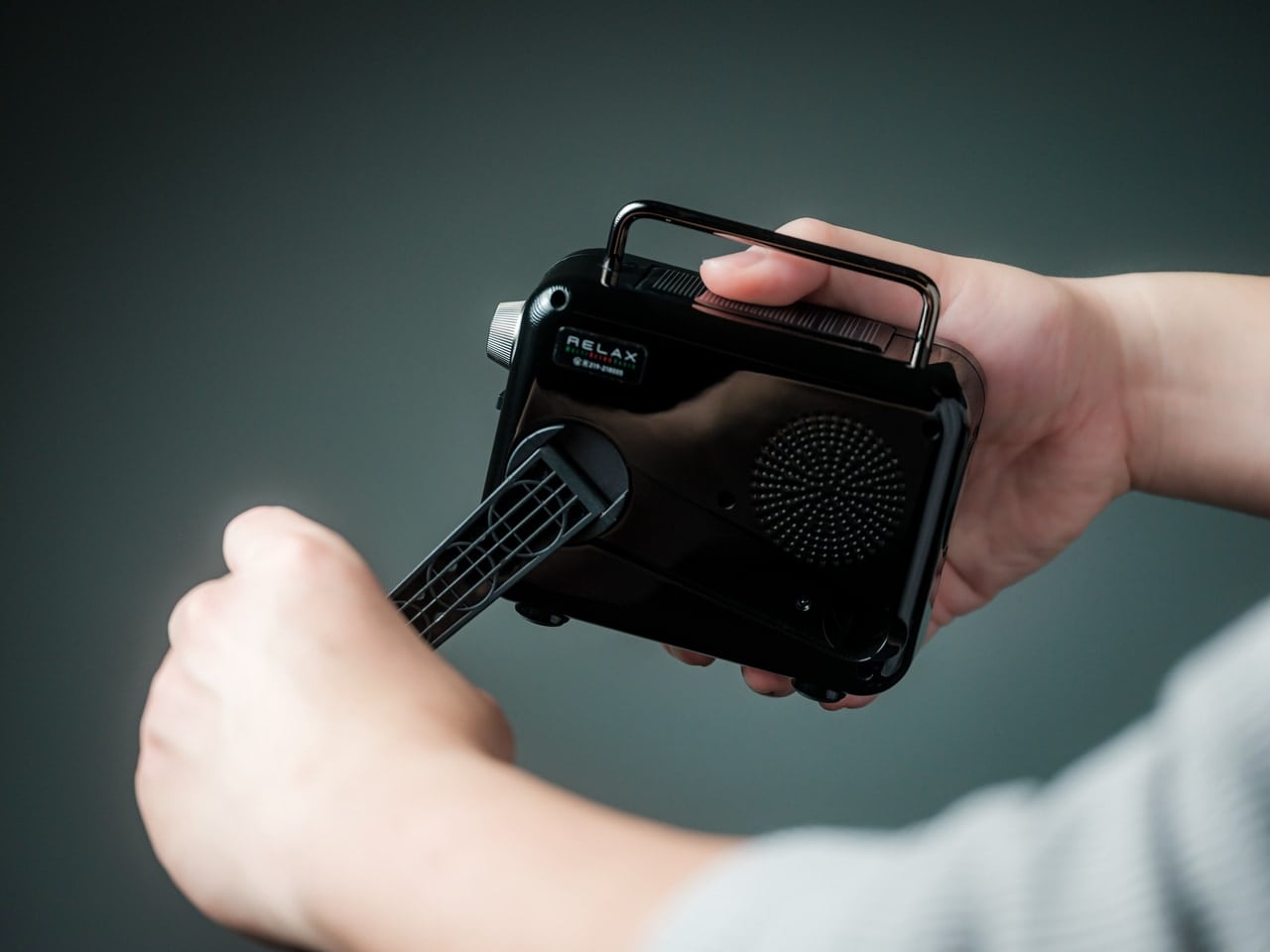 Person holds a small black portable device with a side vent and attached nozzle, held in two hands.