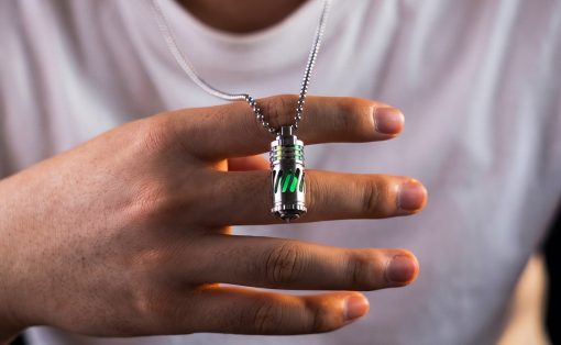 Hand holding a silver futuristic pendant with green glowing panels on a chain.