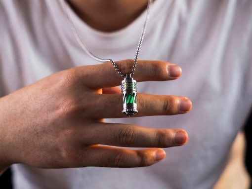 Hand holding a silver futuristic pendant with green glowing panels on a chain.