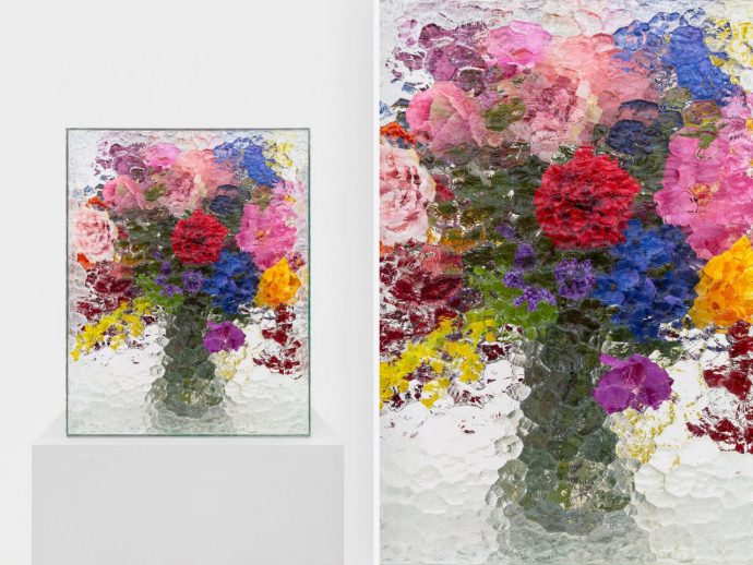 Vibrant, thickly textured floral painting in a glass frame on a white pedestal against a pale background.