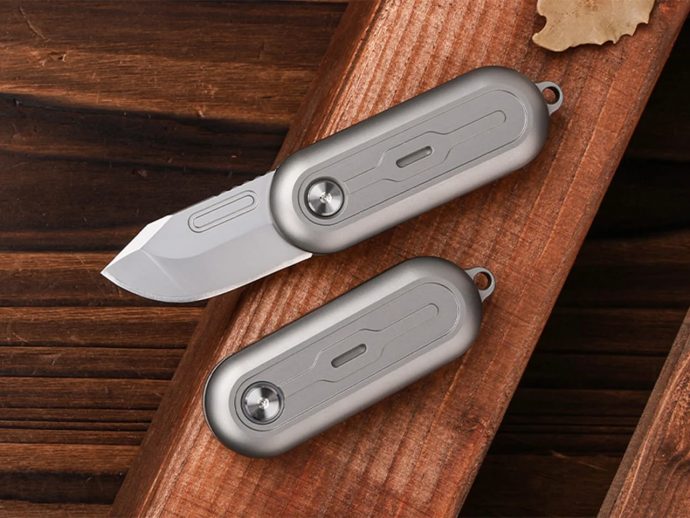 Two gray folding pocket knives on a wood surface, one blade extended.