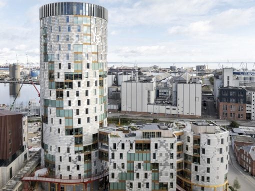 Tall cylindrical modern building with a glass and metal facade beside a harbor and industrial district.