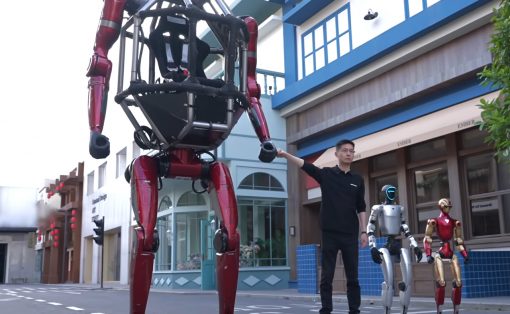 Man in a black shirt gestures toward a towering red humanoid robot on a city street, with silver and gold robots nearby.