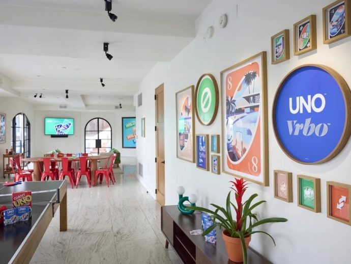 Bright game/lounge area with UNO-themed wall art, red metal chairs around a long table, and a ping-pong table on the left.