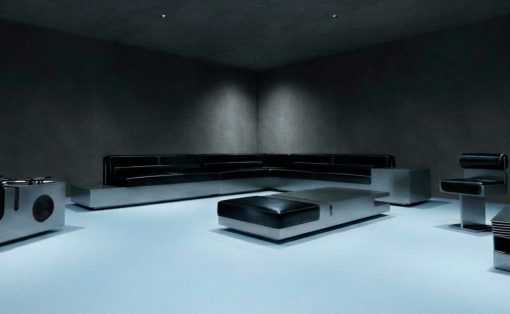 Dark minimalist living room with a black sectional sofa, low square ottoman, and sleek metal accents on a bright pale floor.