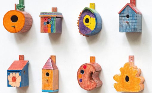 Eight colorful wooden birdhouses mounted on a white wall, each with a unique shape and hand-painted design.