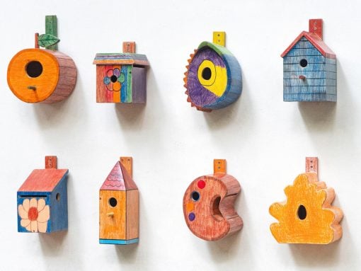 Eight colorful wooden birdhouses mounted on a white wall, each with a unique shape and hand-painted design.