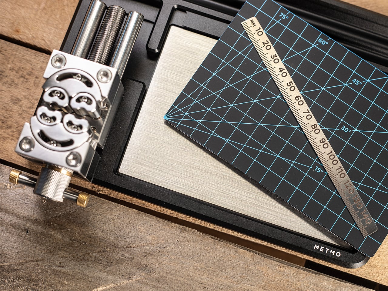 Close-up of a metal hole-punch tool on a wooden workbench, beside a blue-grid cutting mat with a wooden ruler laid diagonally across it.