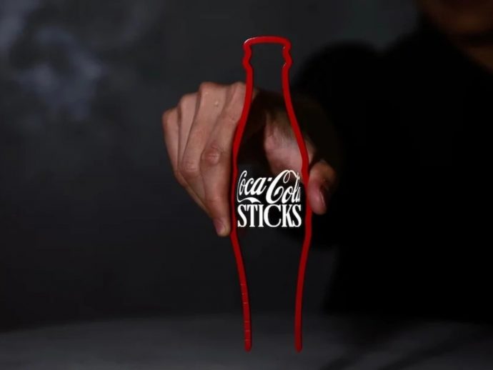 Hand gripping a Coca-Cola bottle outline drawn in red, with the text 'Coca-Cola STICKS' visible on the bottle