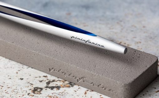 A metal knife blade resting on a grey whetstone used for sharpening, with a blue edge visible along the blade.