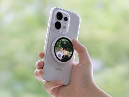 Hand holding a light gray OPPO smartphone with a circular photo display on the back, outdoors with a green blurred background.