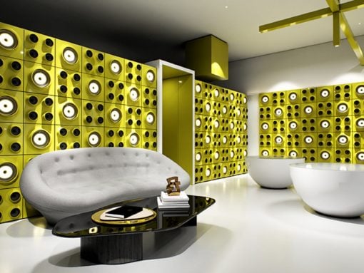 Modern lounge with bold yellow geometric wall panels, a white curved sofa, and a glossy black coffee table.