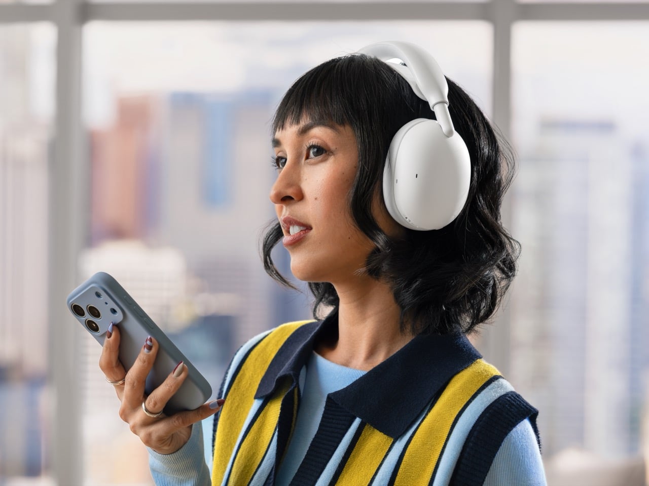 Woman wearing off-white Logitech Zone Vibe Pro headphones while holding a smartphone
