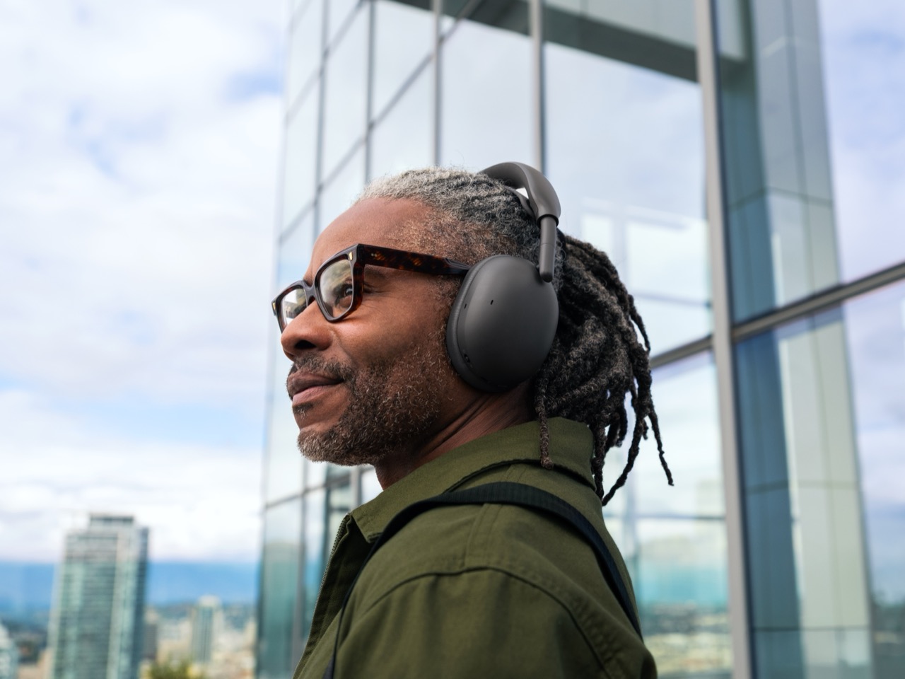 Man wearing graphite Logitech Zone Vibe Pro headphones outdoors near a glass building